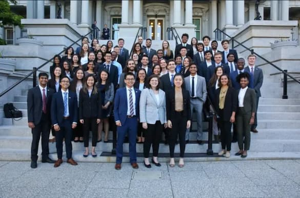 Many rows of young people on the steps of a federal building wearing suits and smiling towards the camera